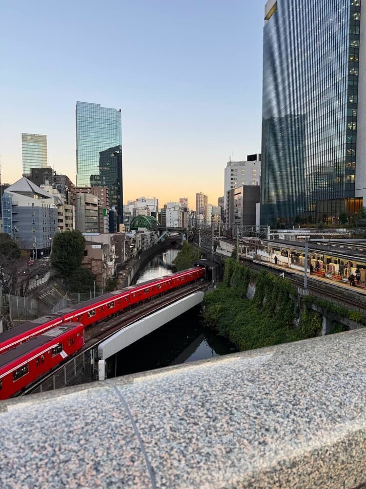 A red Tokyo Metro train crossing the river at Ochanomizu, towers behind it
